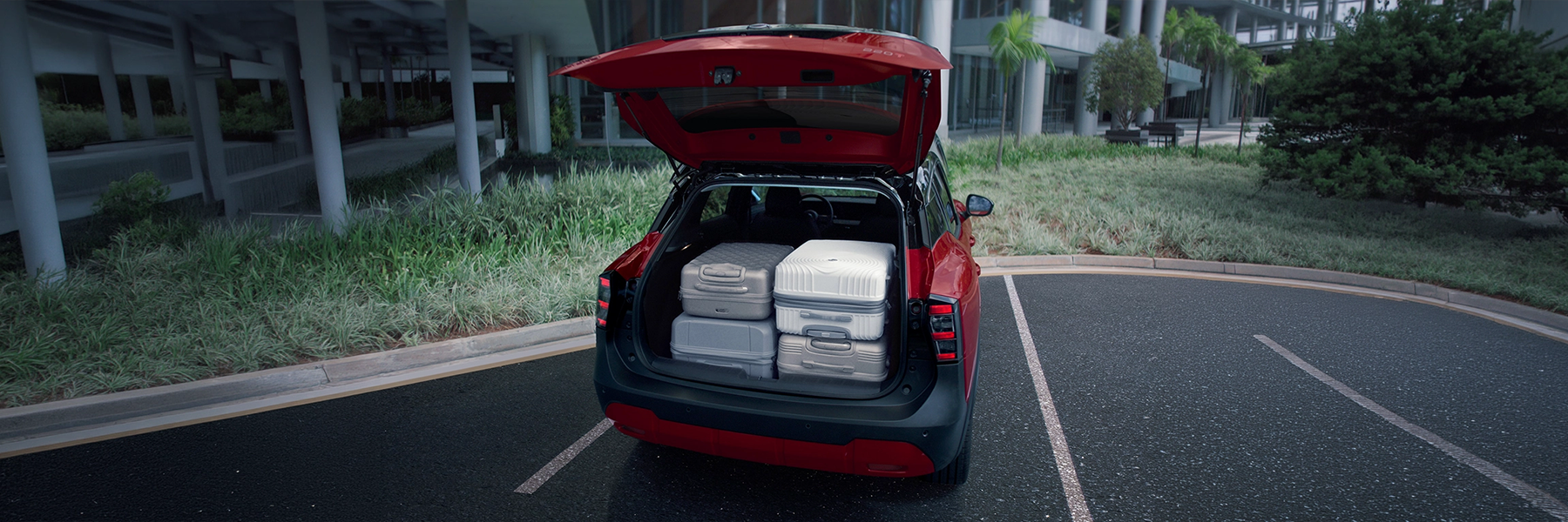 Novo Nissan Kicks vermelho com o porta-malas aberto, acomodando quatro malas de viagem, demonstrando a capacidade de carga.
