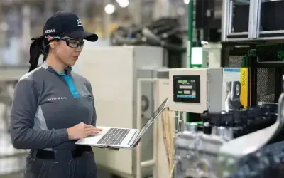 Engenheira da Nissan em uma fábrica, usando equipamentos de proteção e laptop. A imagem mostra a aplicação de tecnologia para modernizar processos de produção.
