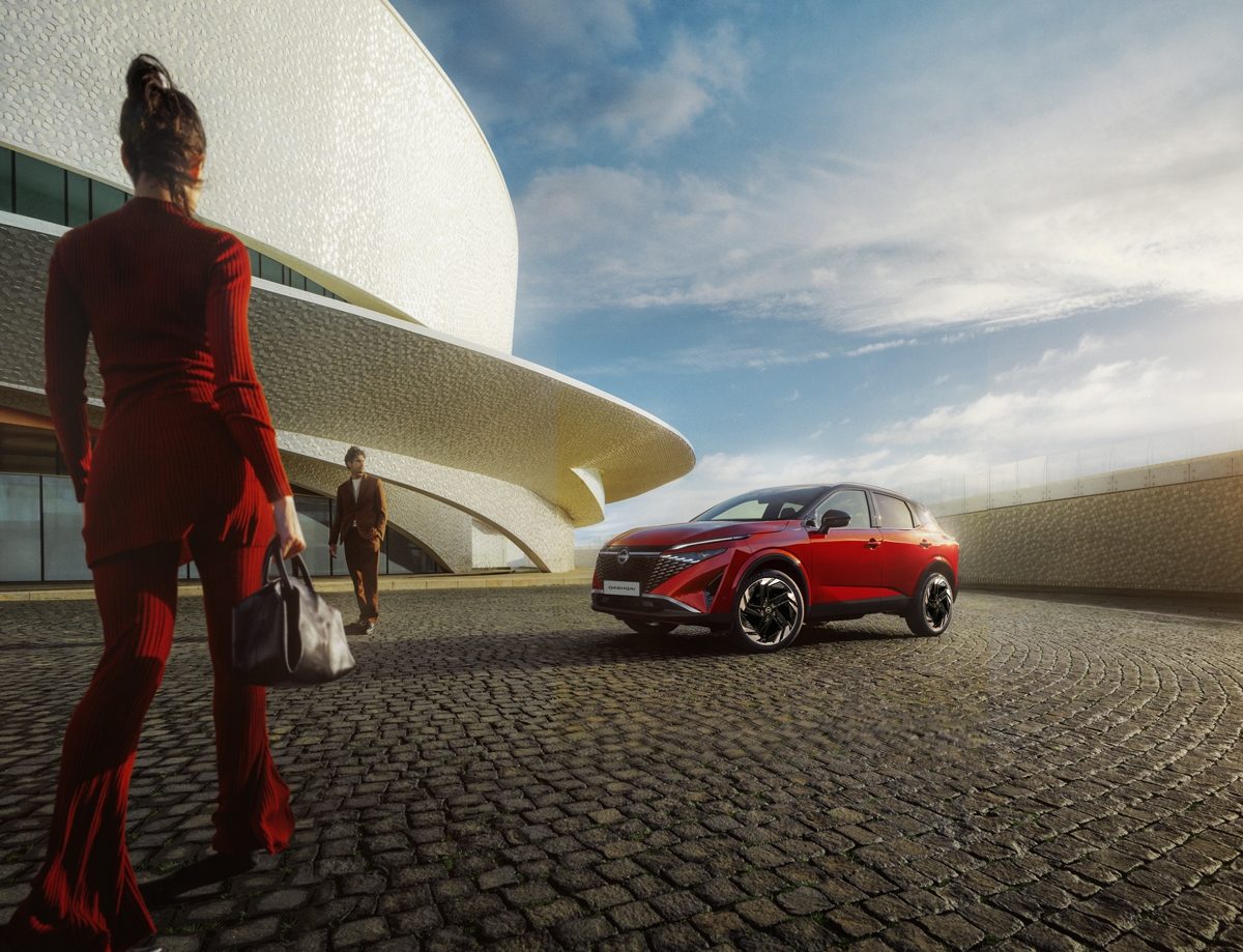 Nissan Qashqai e-Power 3/4 front static shot in front of building with woman walking towards car - Hybrid SUV