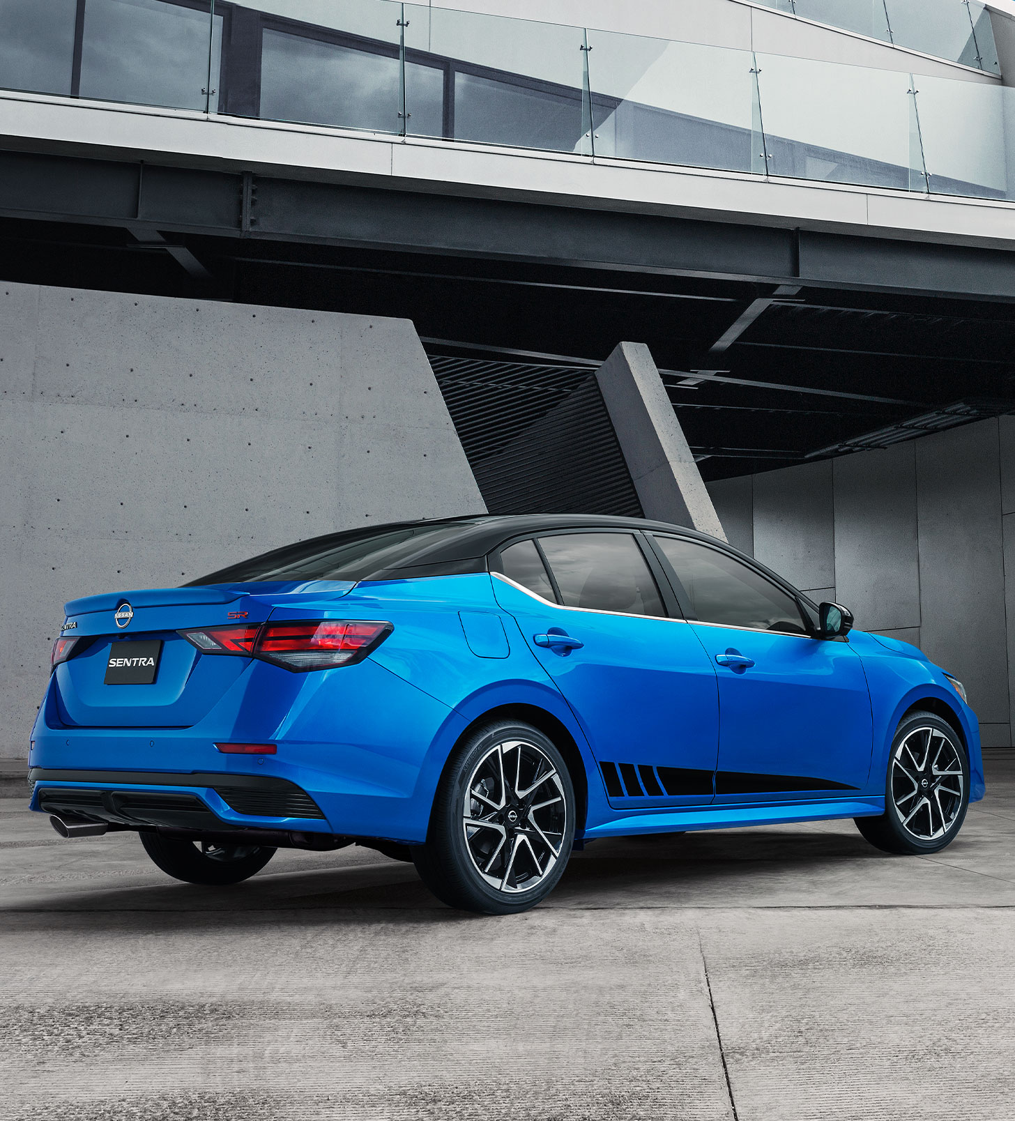 El Nissan Sentra en azul resplandece bajo una estructura moderna, reflejando la confianza que brindan sus planes de mantenimiento prepagados.