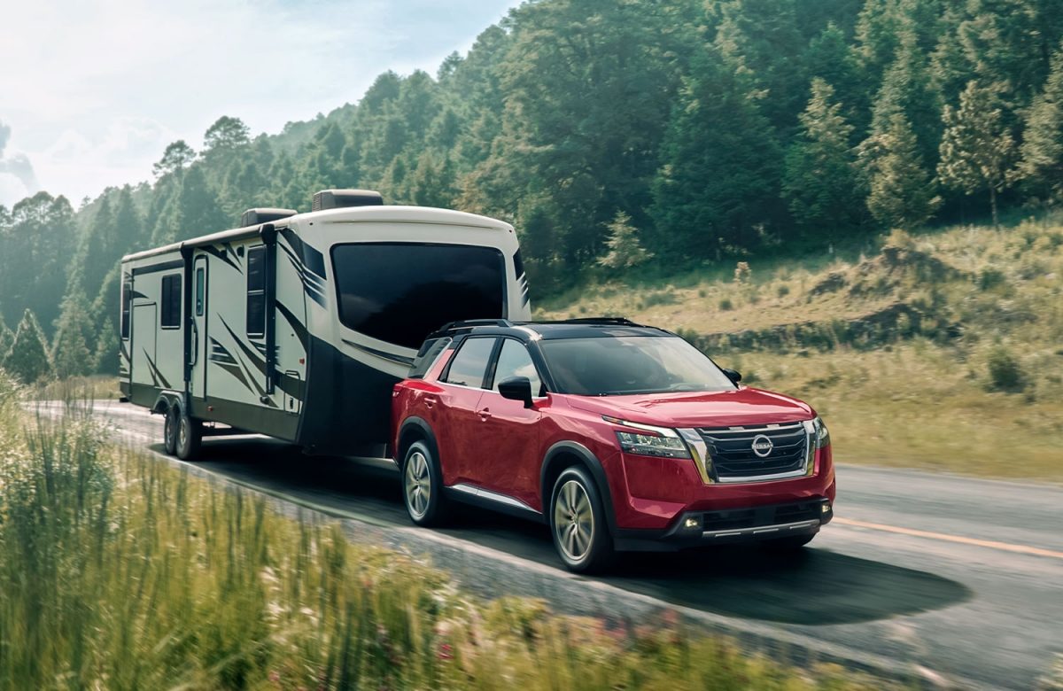 El nuevo Nissan Pathfinder demostrando su capacidad de remolque lleva un camper a través de una carretera con un espeso bosque de fondo