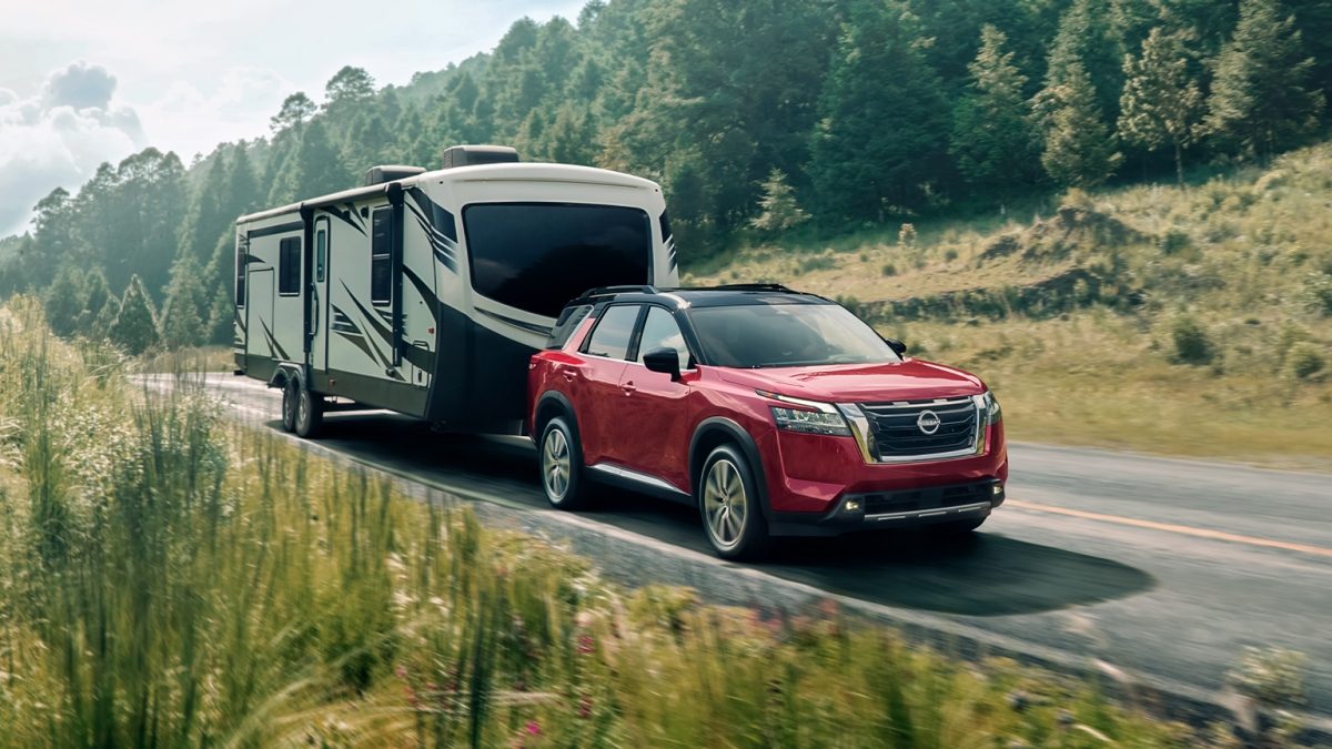 El nuevo Nissan Pathfinder demostrando su capacidad de remolque lleva un camper a través de una carretera con un espeso bosque de fondo