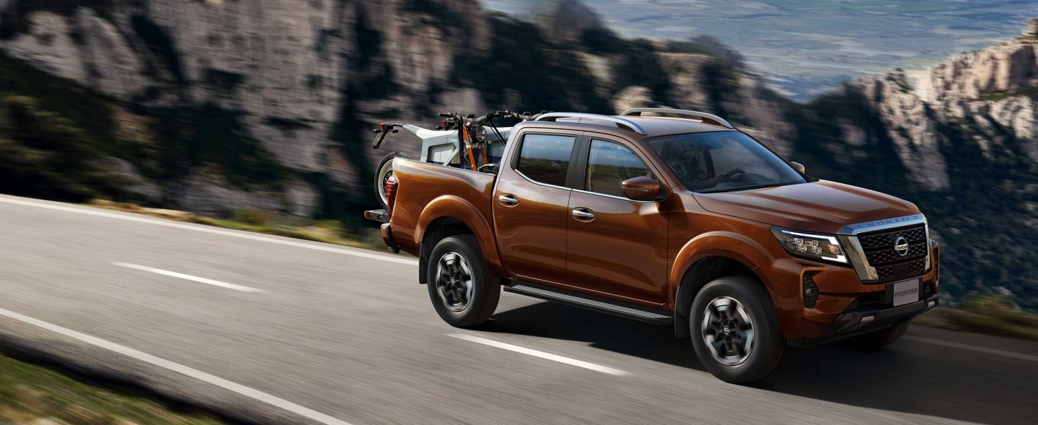 2021 Nissan Frontier driving on a road with off-road motorcycles in the bed