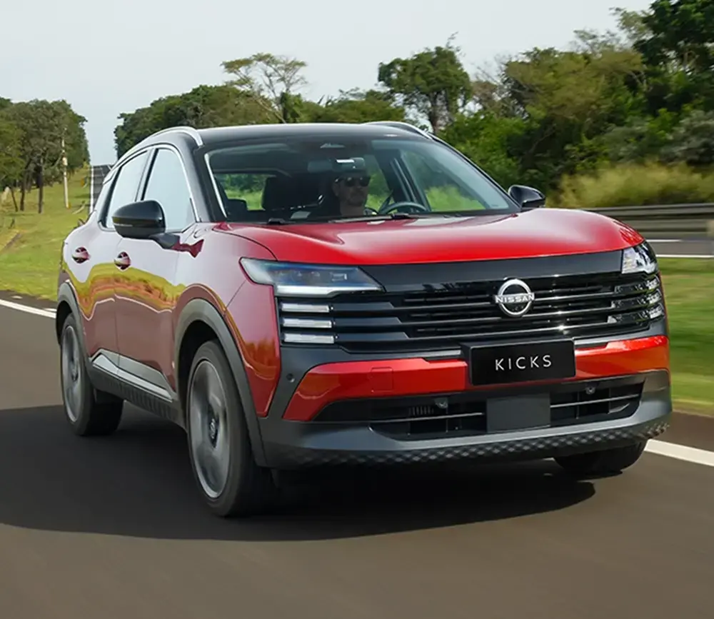Visão frontal em ângulo do SUV Nissan Kicks vermelho com teto preto em movimento em uma pista de testes.