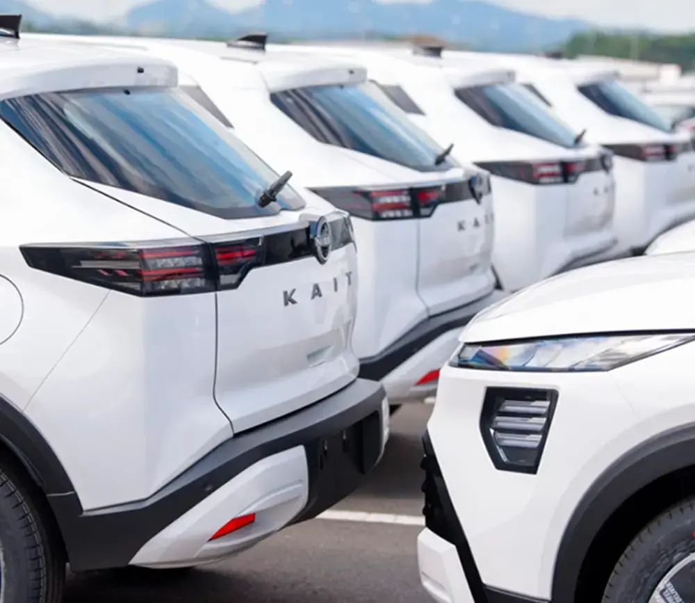 Detalhe da traseira de vários veículos Nissan Kait brancos alinhados em um pátio.