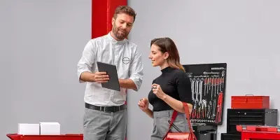Consultor de serviços da Nissan a mostrar informações num tablet a uma cliente numa oficina mecânica com um painel de ferramentas ao fundo