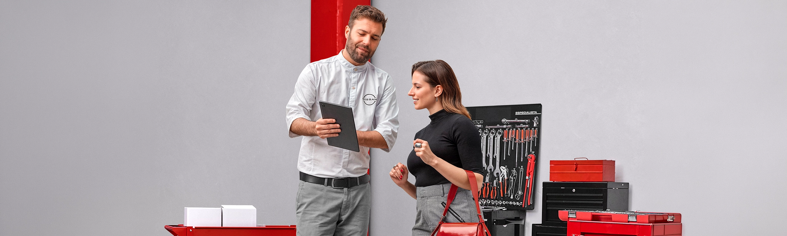 Consultor de serviços da Nissan a mostrar informações num tablet a uma cliente numa oficina mecânica com um painel de ferramentas ao fundo.