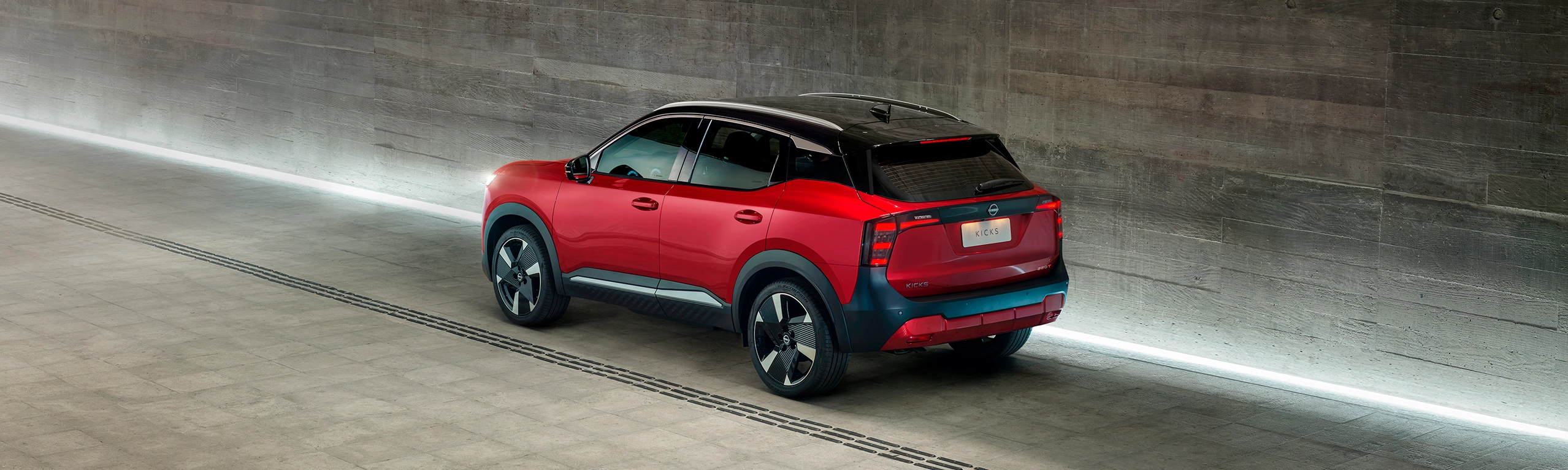 SUV Nissan Kicks vermelho com teto preto visto de trás em um túnel de concreto moderno e iluminado.