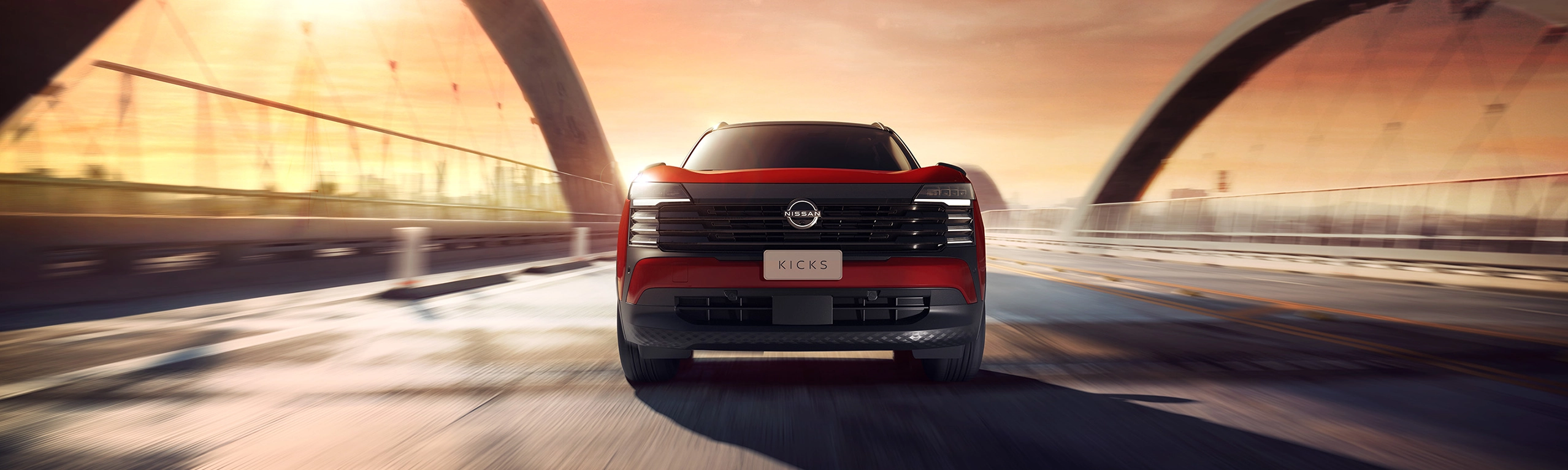 Nissan Kicks vermelho com teto preto em movimento por uma rua urbana, visto pelo ângulo dianteiro, com placa escrita Kicks. 