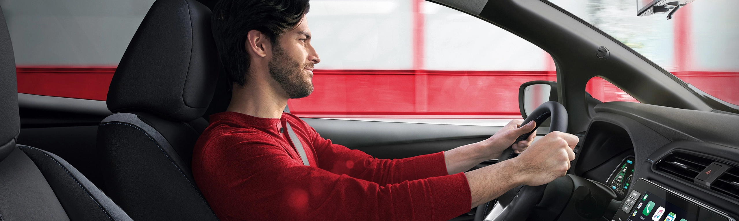 Homem de camisa vermelha segurando o volante de um carro em movimento, com um borrão de velocidade vermelho e branco visível fora da janela.