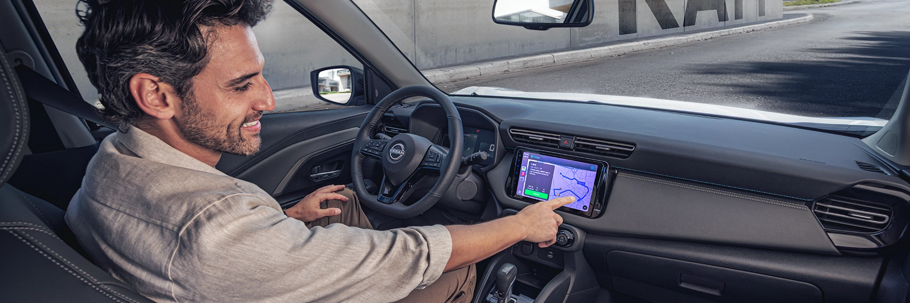 Homem sorrindo no banco do motorista de um Nissan, tocando na tela multimídia que exibe um mapa de navegação.