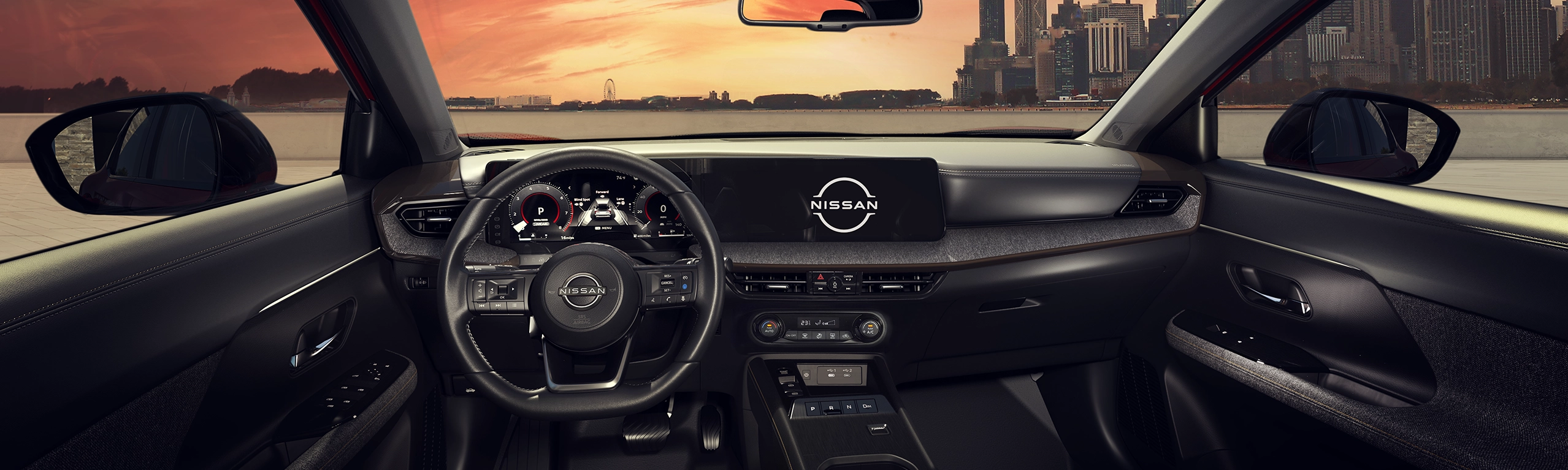 Interior do painel escuro de um carro Nissan Kicks, mostrando o volante e as telas digitais ligadas, com vista pelo para-brisa para uma cidade ao pôr do sol.