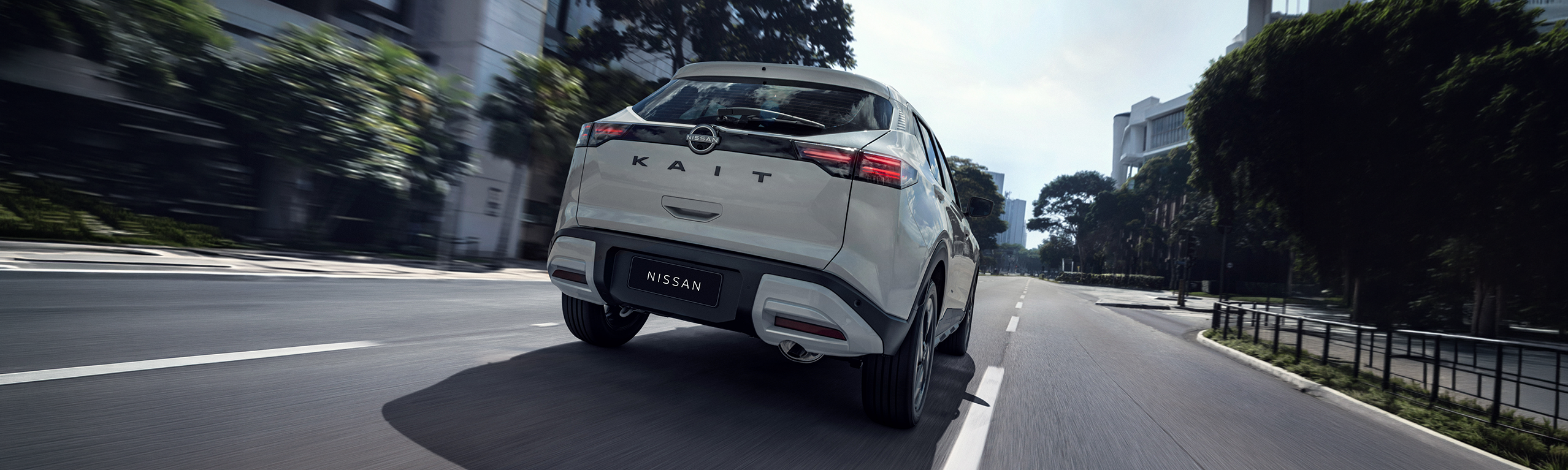 Vista traseira do SUV Nissan Kicks branco em movimento numa avenida da cidade, a destacar o design das luzes traseiras LED e o nome do modelo na porta do bagageiro.