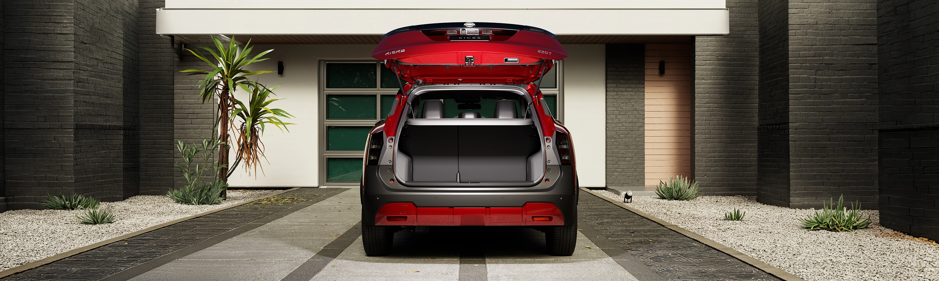 Traseira de SUV vermelho Nissan Kicks com o porta-malas aberto e vazio, estacionado em frente a uma casa moderna.