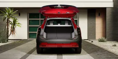 Traseira de SUV vermelho Nissan Kicks com o porta-malas aberto e vazio, estacionado em frente a uma casa moderna.