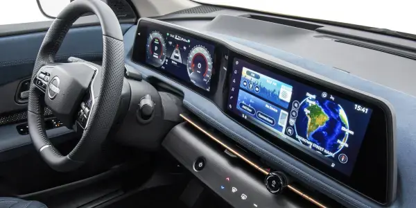 Painel digital duplo do Nissan Ariya, com telas unidas exibindo informações de direção e multimídia. O interior tem acabamento em tecido azul e volante moderno.