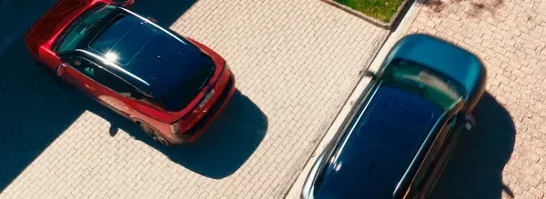 Vista superior de dois carros (um vermelho e um escuro) estacionados em um piso de tijolos. O carro vermelho é um Nissan Kicks.