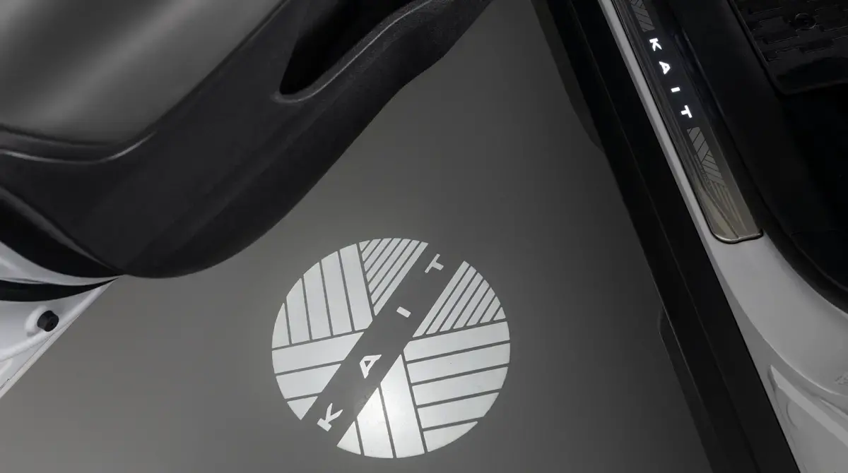 Detalhe da luz projetora do Nissan KAIT no chão, exibindo um logo circular estilizado com a palavra "KAIT" ao abrir a porta.