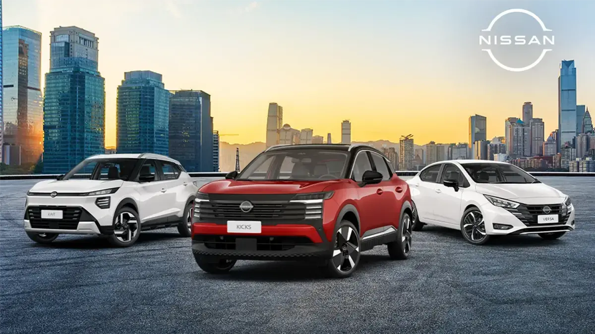 Três carros da Nissan estacionados lado a lado, um Nissan Kait prata, um Kicks vermelho no centro, um Nissan Versa branco, com o horizonte de uma cidade ao pôr do sol ao fundo.