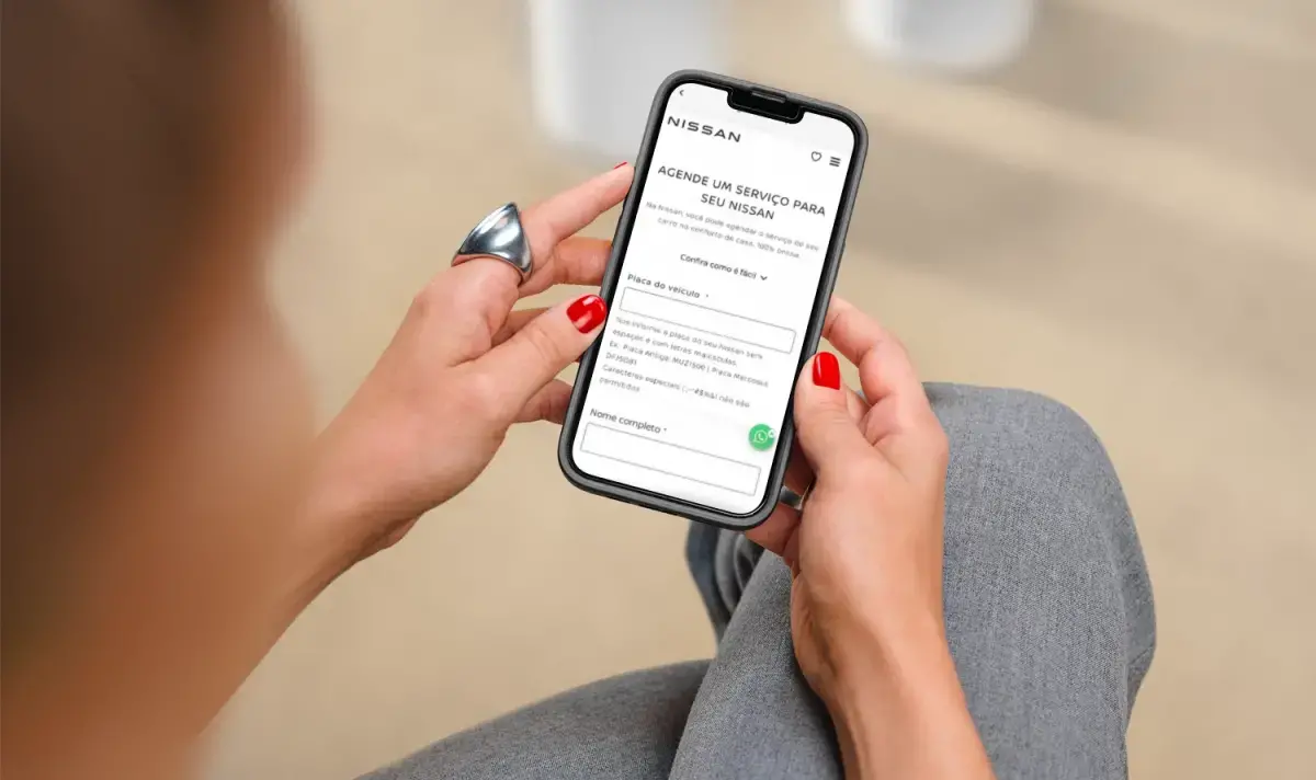 Pessoa segurando um celular exibindo uma página de manutenção preventiva da Nissan. Demonstra a importância da manutenção para veículos.