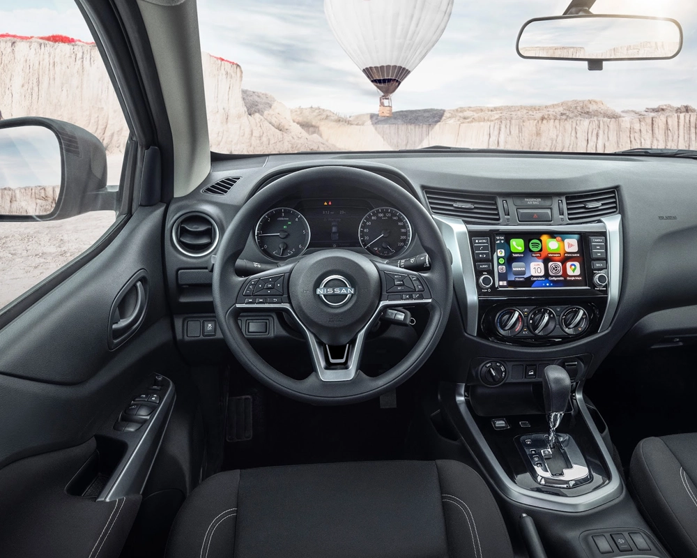 Vista interna de um veículo Nissan, destacando o painel, volante e sistema multimídia com mostradores e controles.