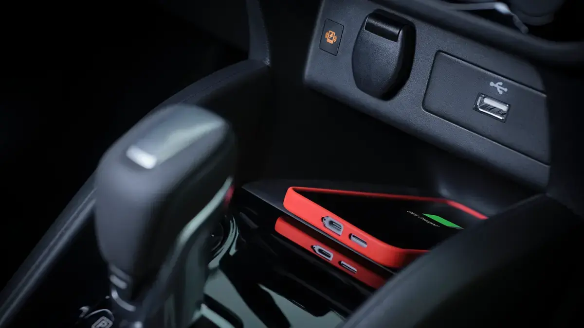 Close-up do carregador de celular por indução (sem fio) com um smartphone vermelho e porta USB no Nissan KAIT.