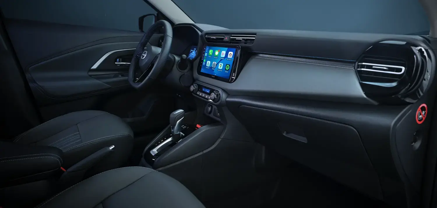 Vista do cockpit do Nissan KAIT. Destaque para o volante, painel de instrumentos digital e a tela multimídia central, com interior escuro e moderno.