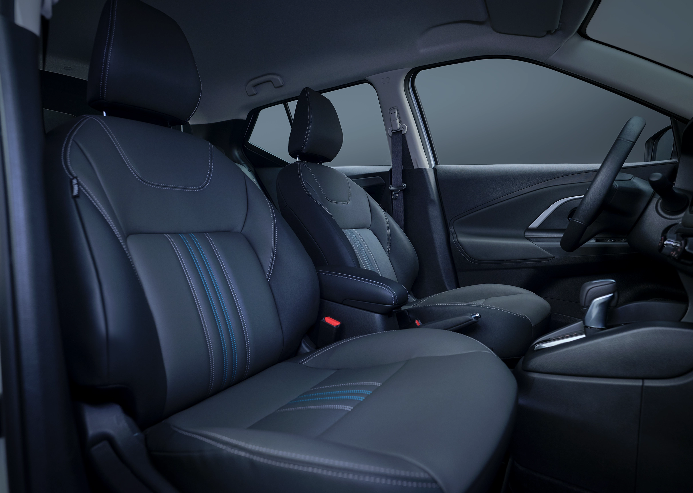 Interior do Nissan KAIT com foco nos bancos dianteiros em material preto com costuras decorativas em azul-claro. O console central e o seletor de marchas são visíveis.