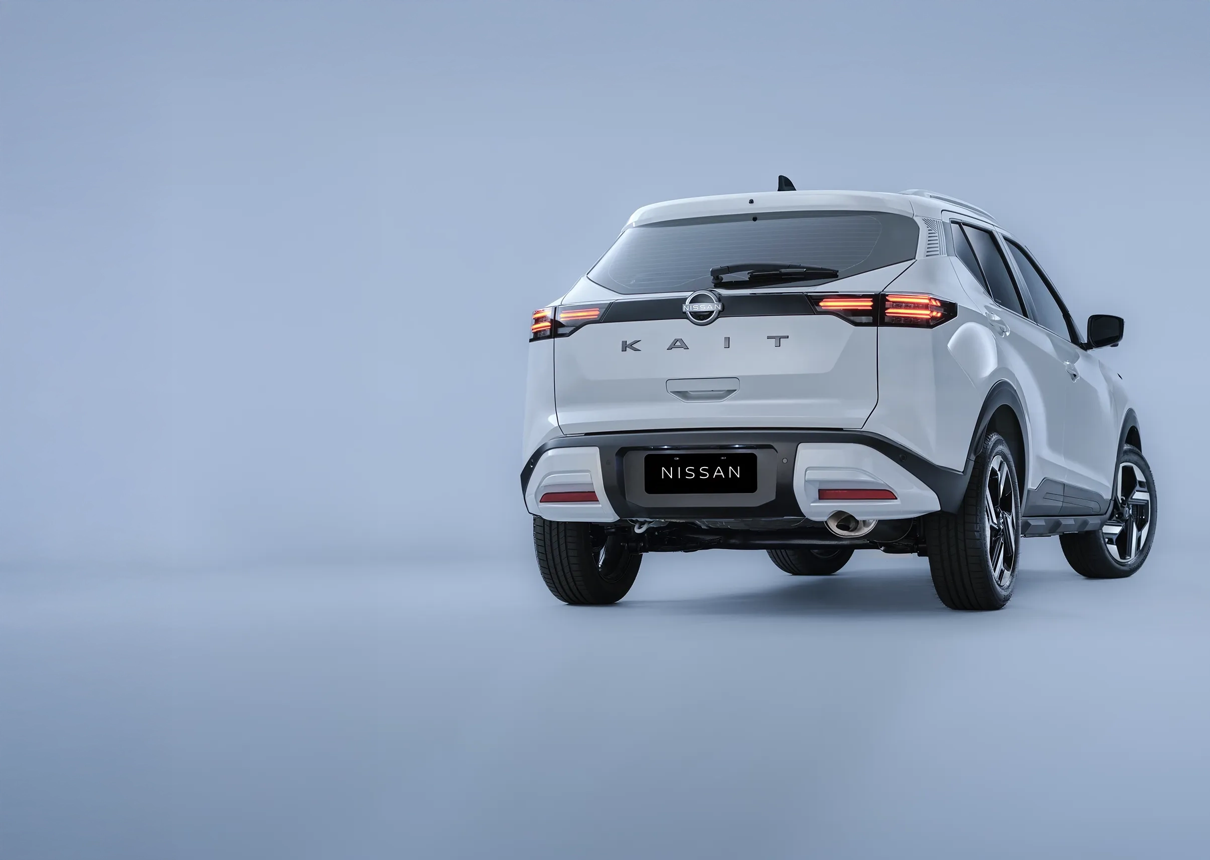 ista traseira de um Nissan KAIT branco estacionado em frente a uma residência de arquitetura moderna. As lanternas traseiras horizontais e o emblema "KAIT" são visíveis.
