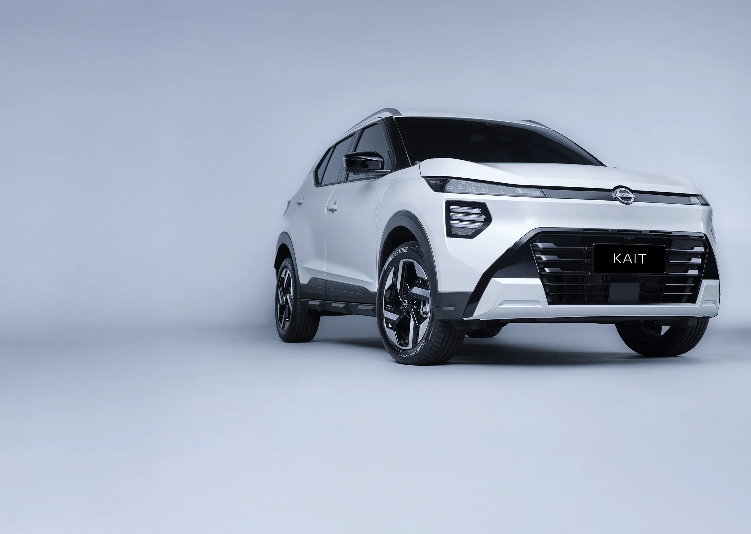 Vista frontal de baixo de um SUV Nissan KAIT branco estacionado em frente a uma residência moderna com diferentes texturas. O design frontal angular e as luzes são destacados.