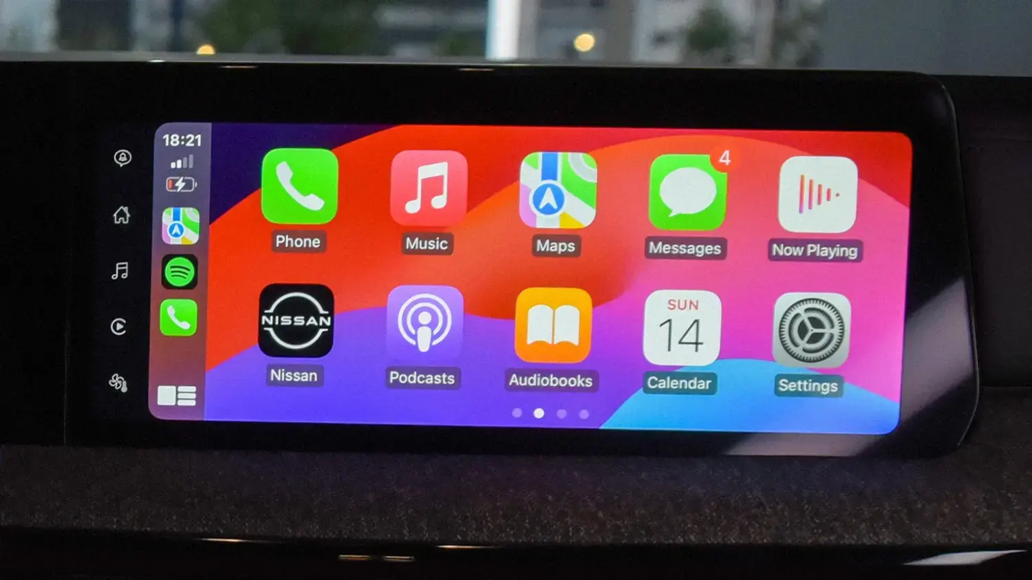 Tela da central multimídia de um Nissan Kicks exibindo a interface do Apple CarPlay, com diversos ícones de aplicativos coloridos organizados em grade, incluindo "Phone", "Music", "Maps" e "Calendar". O horário "18:21" e a data "SUN 14" são visíveis na barra superior.