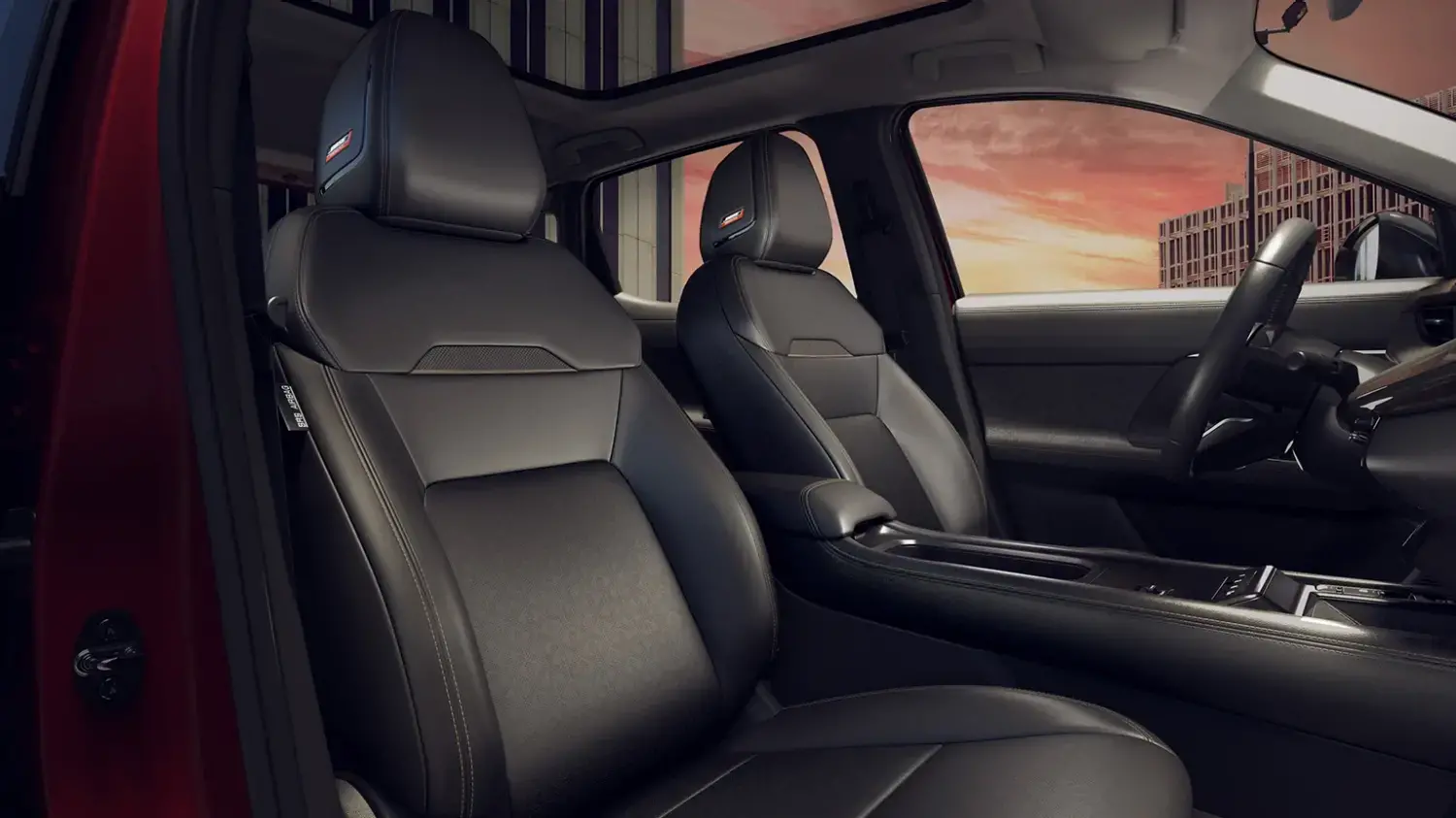 Interior de um Nissan Kicks com foco nos bancos dianteiros em couro preto, que apresentam detalhes em costura e um emblema nos encostos de cabeça. Um teto solar panorâmico é visível acima, com a paisagem urbana ao fundo.