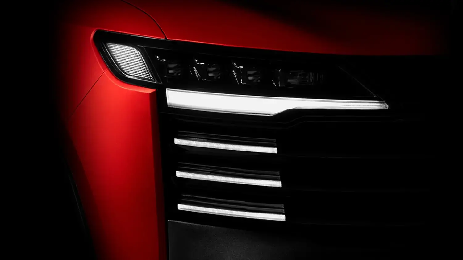 Close-up dos faróis dianteiros de LED do Nissan Kicks vermelho, com as luzes diurnas horizontais acesas, integradas de forma elegante à grade frontal preta do veículo, realçando seu olhar moderno e tecnológico.