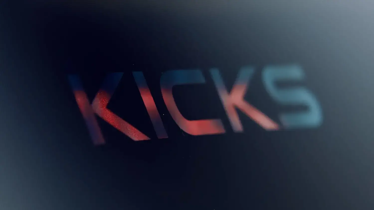 Logo estilizado "KICKS" em tipografia moderna com gradiente de cor vibrante em tons de vermelho e azul sobre um fundo escuro, simbolizando o novo e reimaginado design do Nissan Kicks.