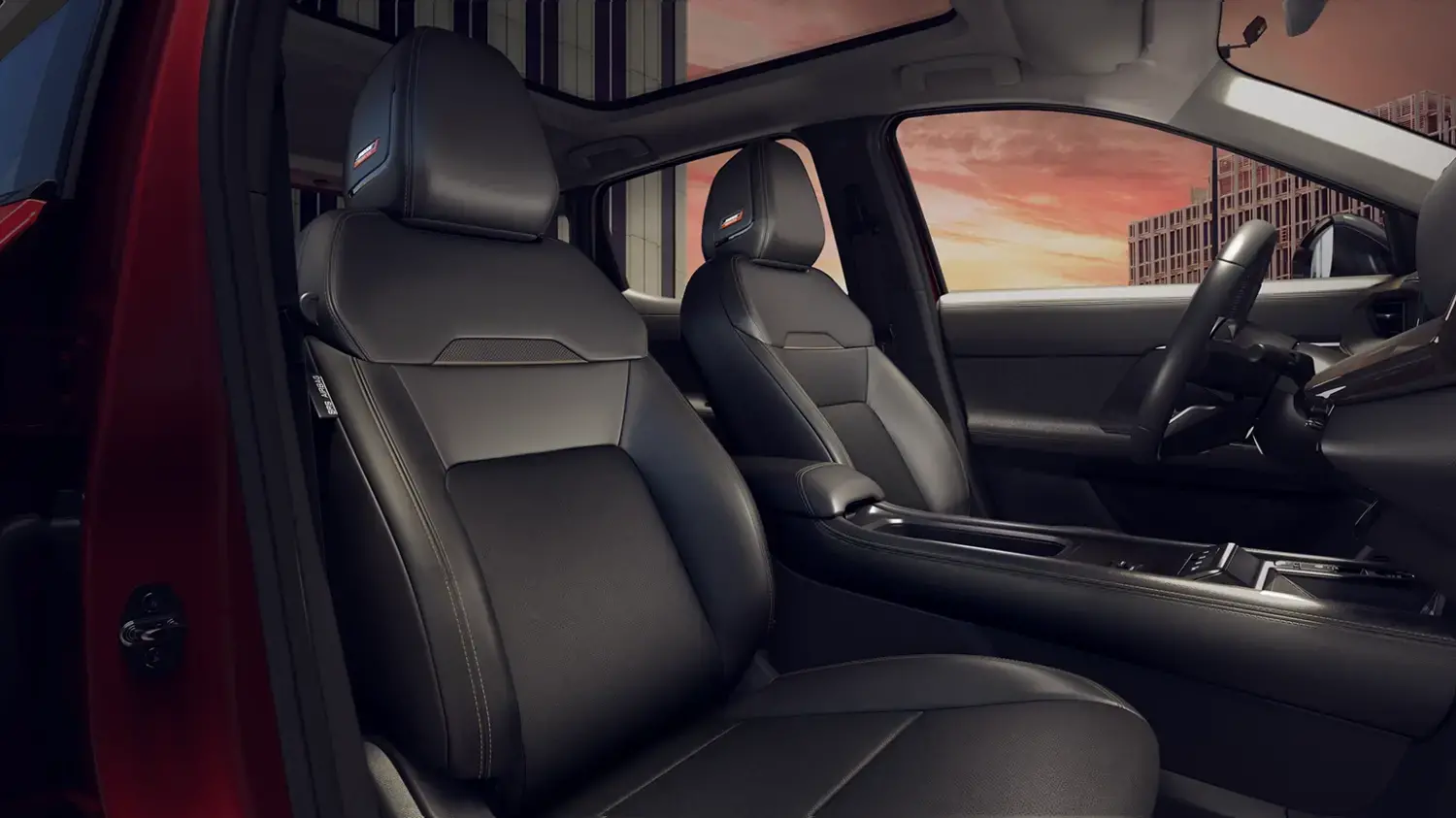Interior de um Nissan Kicks com foco nos bancos dianteiros em couro preto, que apresentam detalhes em costura e um emblema nos encostos de cabeça. Um teto solar panorâmico é visível acima, com a paisagem urbana ao fundo.