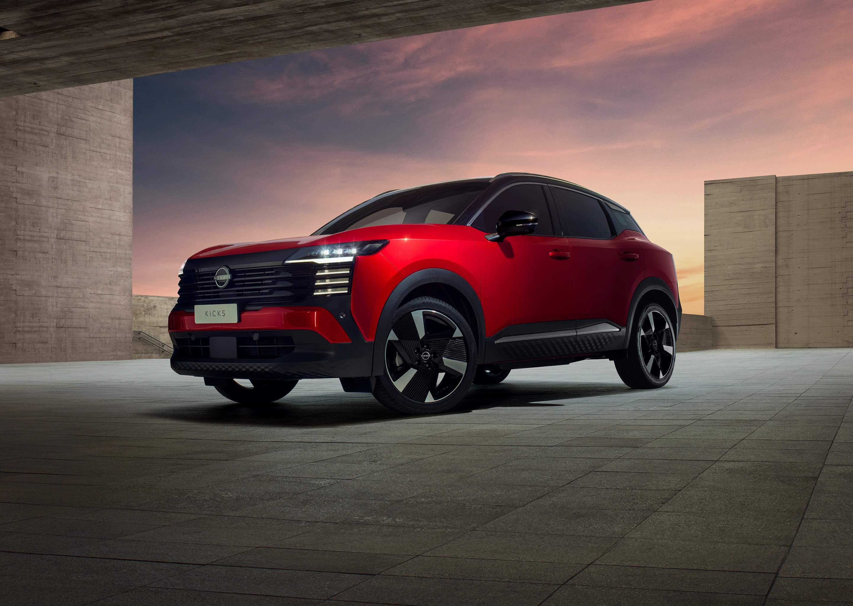 Visão traseira do SUV Nissan Kicks vermelho com teto preto, com a visão frontal, parado com uma vista do céu ao fundo.