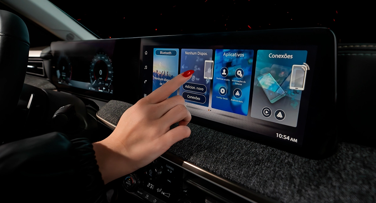 Close-up do painel central de um Nissan Kicks, mostrando a tela multimídia digital com um mapa, abaixo da qual estão os controles físicos do ar-condicionado com mostradores. 