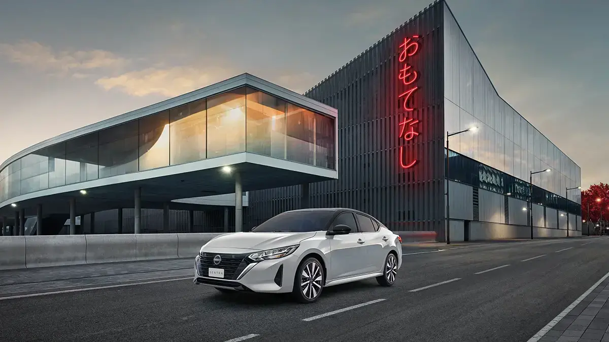 Um carro Nissan Sentra branco estacionado em uma rua moderna, com arte urbana e um homem observando ao fundo.