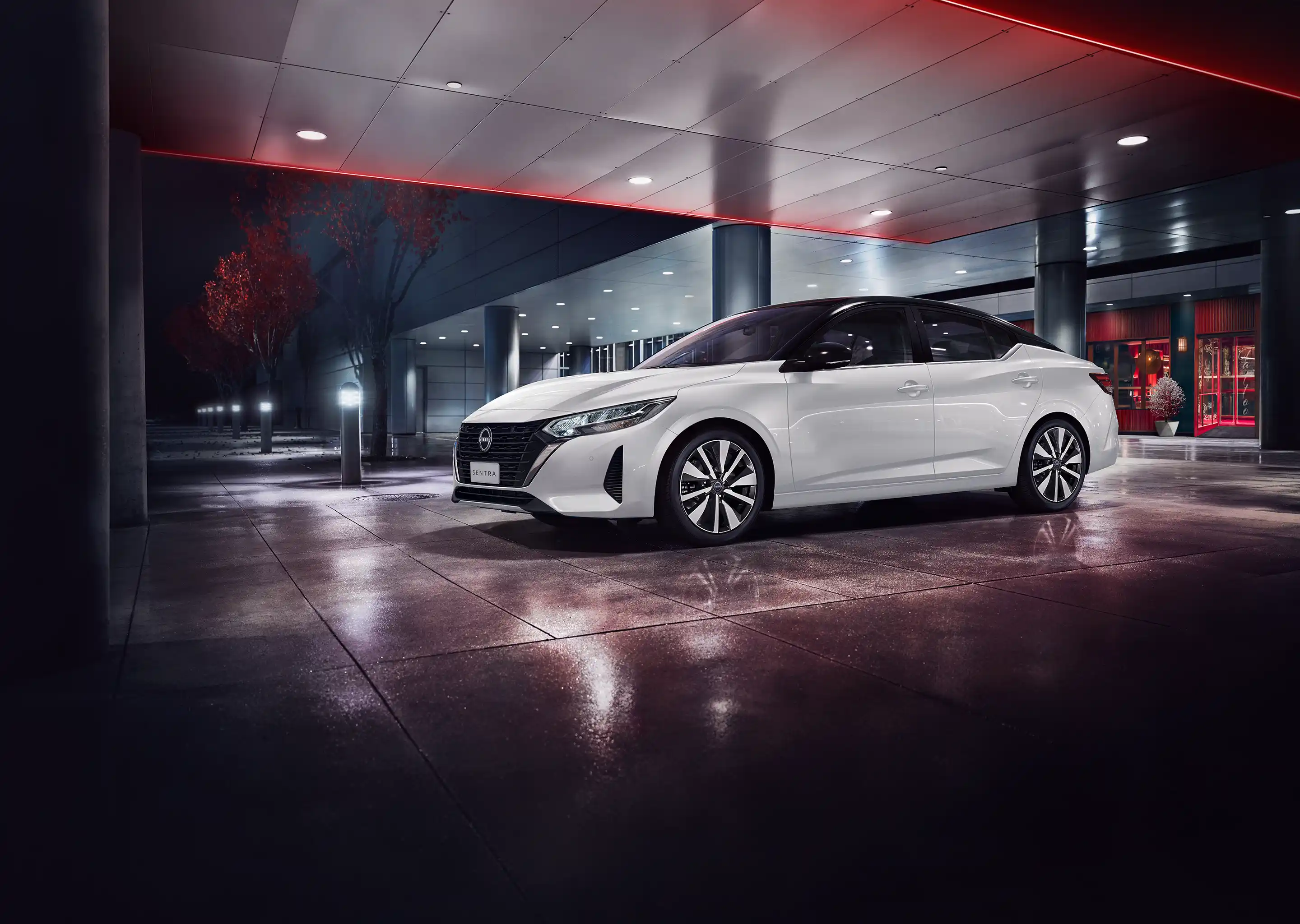 Nissan Sentra branco posicionado em uma rua urbana com uma fachada moderna ao fundo.