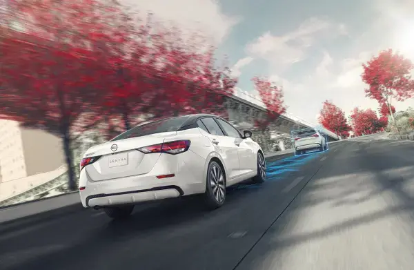 Carro Nissan Sentra branco parado na faixa de pedestres com uma faixa azul a sua frente, enquanto um homem atravessa a faixa falando no celular.