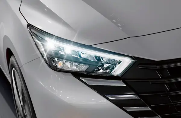 Detalhe do farol de um Nissan Versa branco, destacando o design e a iluminação sofisticada.