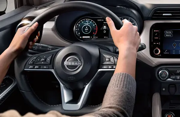 Mãos segurando o volante de um carro Nissan, destacando a tecnologia avançada e o design moderno do painel de instrumentos.