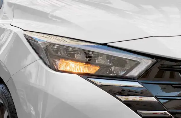 Detalhe do farol de um Nissan Versa branco, destacando o design e a iluminação sofisticada.