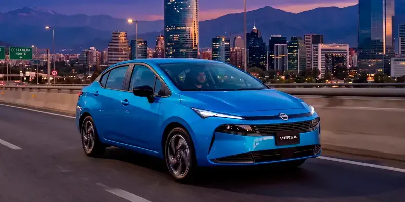 Nuevo Nissan Versa azul circulando por autopista urbana de noche con skyline de Santiago al fondo, destacando su rendimiento en ciudad.