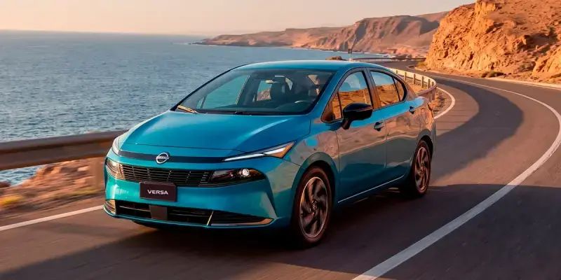 Nuevo Nissan Versa azul circulando por carretera costera al atardecer, destacando su eficiencia en consumo de combustible.