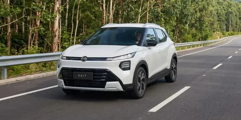 Nissan Kait 2026 blanco circulando por carretera rodeada de vegetación, de frente y en movimiento.