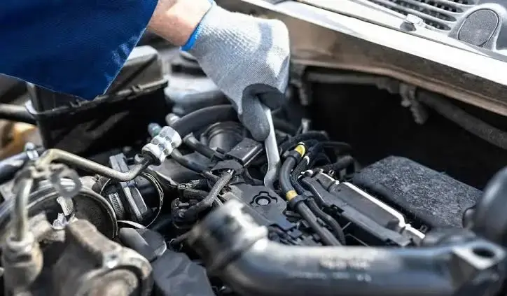 Mecánico con guante revisando el motor de un vehículo durante un mantenimiento preventivo