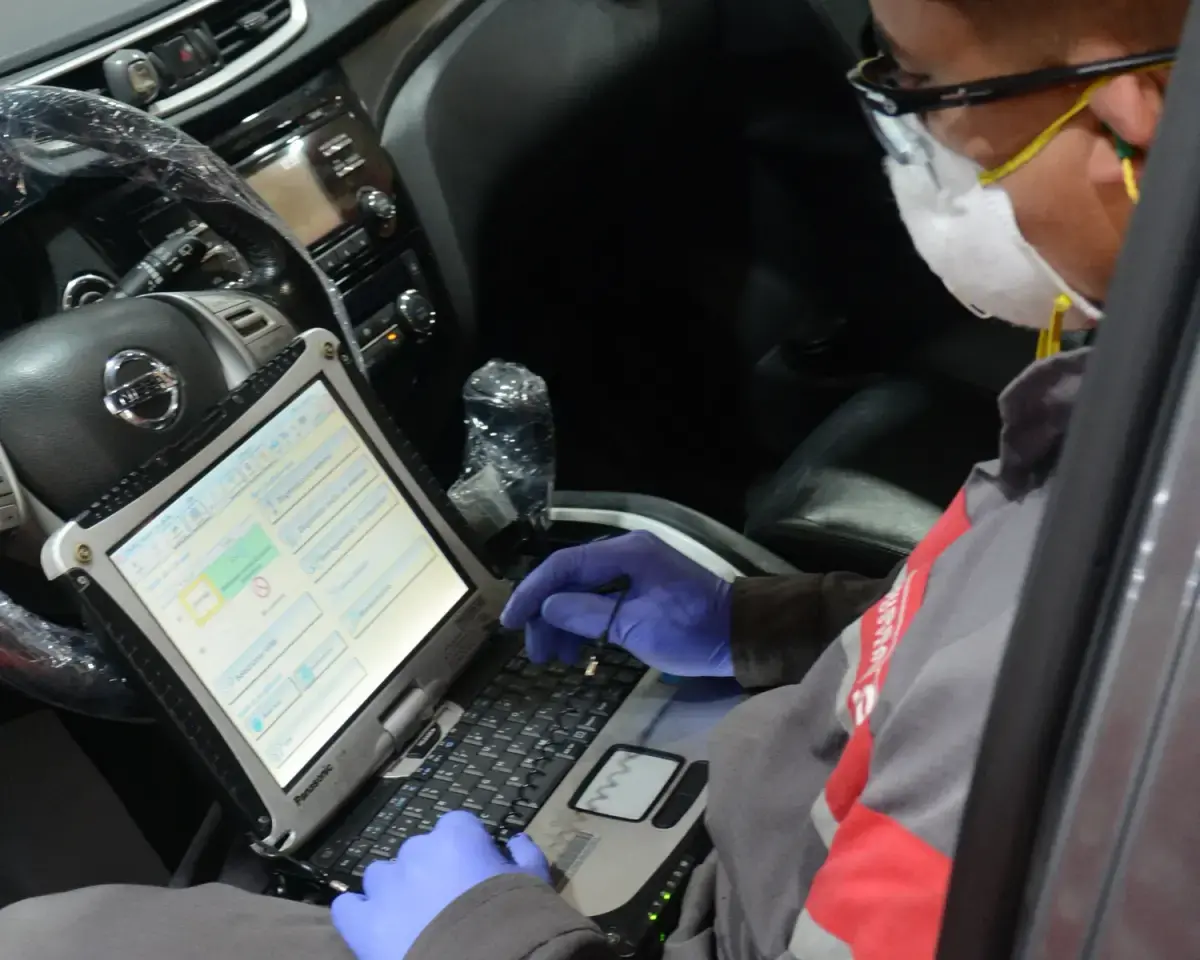 Vista lateral de Nissan ALTIMA rojo merlot con asesores de servicio dando mantenimiento con llantas a full de pantalla.